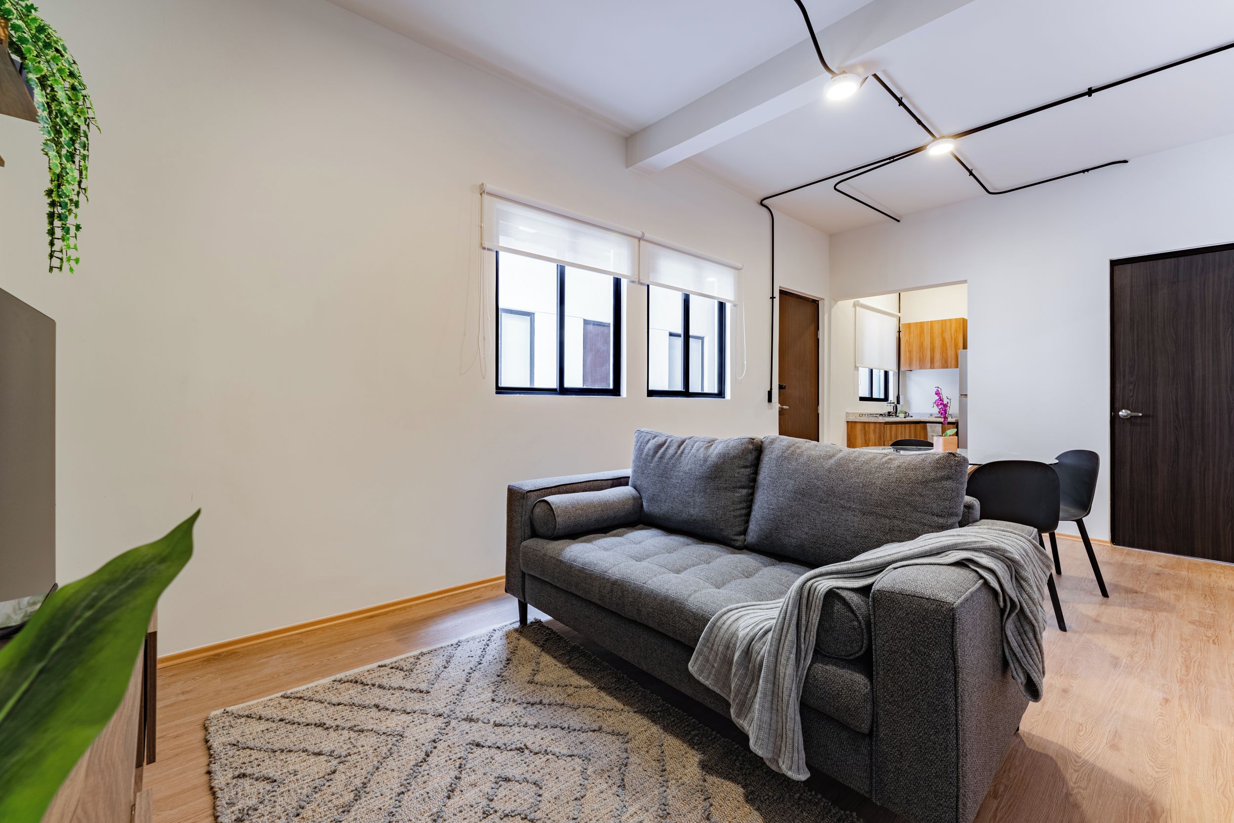 A modern living room with a grey sofa, a wooden floor, and a large window with blinds.