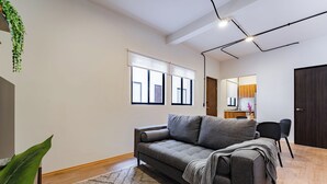 A modern living room with a grey sofa, a wooden floor, and a large window with blinds.
