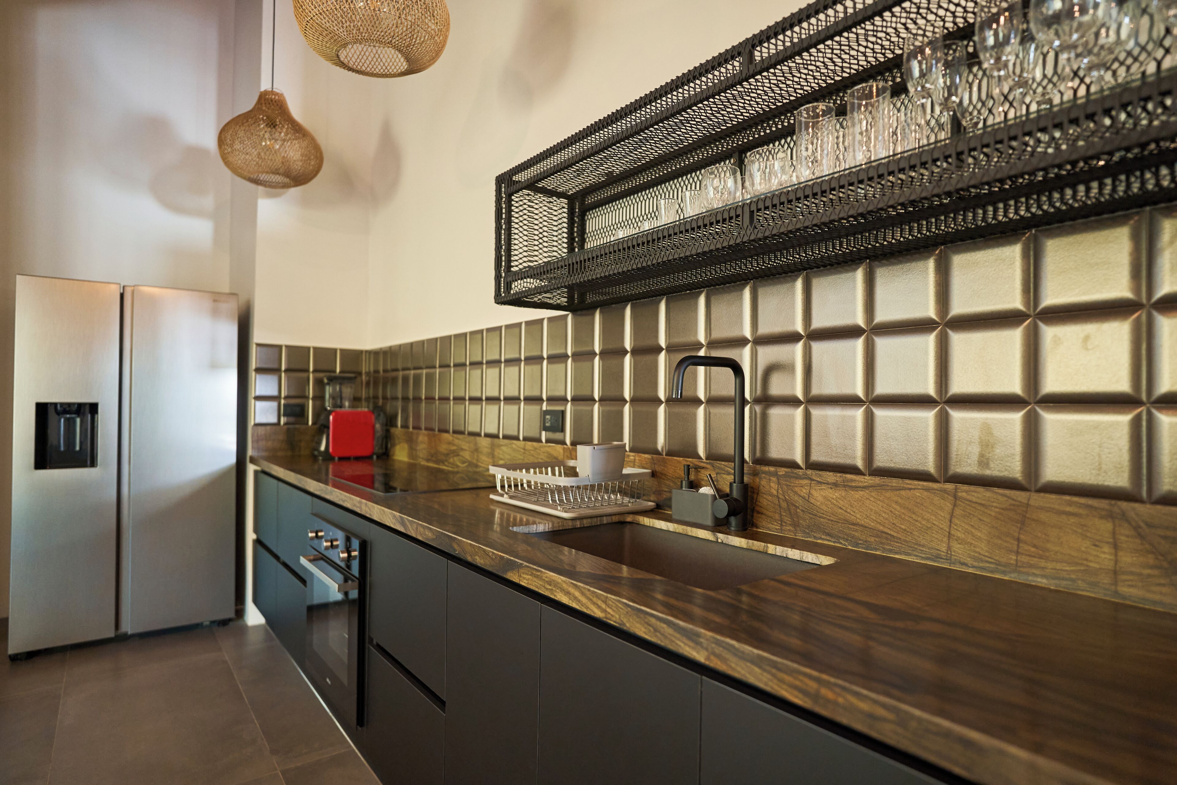 A modern kitchen with a stainless steel refrigerator, a built-in oven, a sink with a faucet, and a countertop with a dish rack.