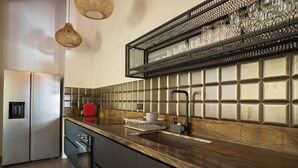 A modern kitchen with a stainless steel refrigerator, a built-in oven, a sink with a faucet, and a countertop with a dish rack. - Desiree Luxury Apartamentos (Malpaís)