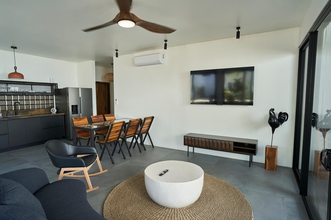 A modern living space with a dining area, a seating area with a round coffee table, and a television mounted on the wall.