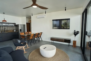 A modern living space with a dining area, a seating area with a round coffee table, and a television mounted on the wall. - Desiree Luxury Apartamentos (Malpaís)