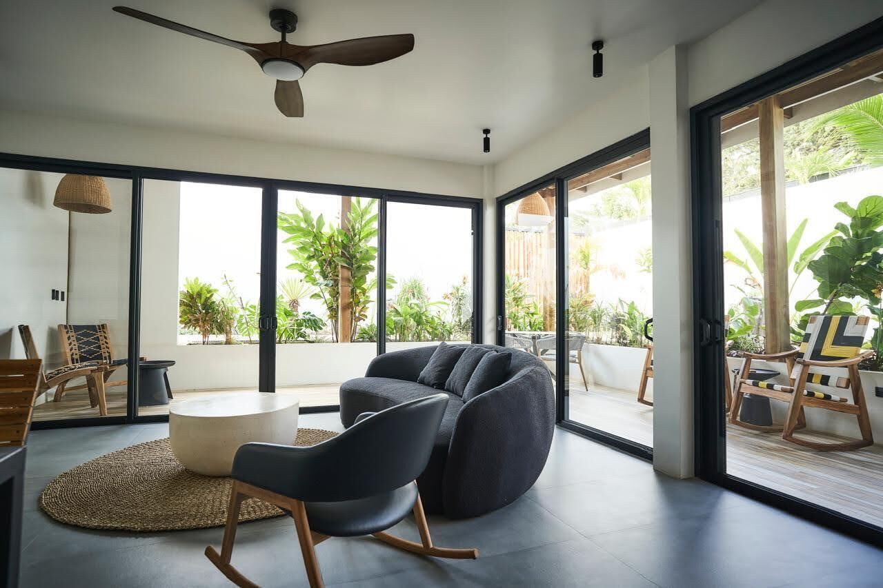 A modern living room with a large window, a ceiling fan, and a seating area with a round table.
