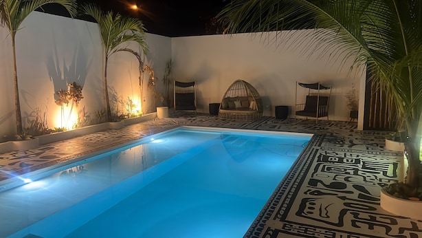 A swimming pool with a geometric patterned floor, surrounded by walls with plants and a hanging chair. - Desiree Luxury Apartamentos (Malpaís)