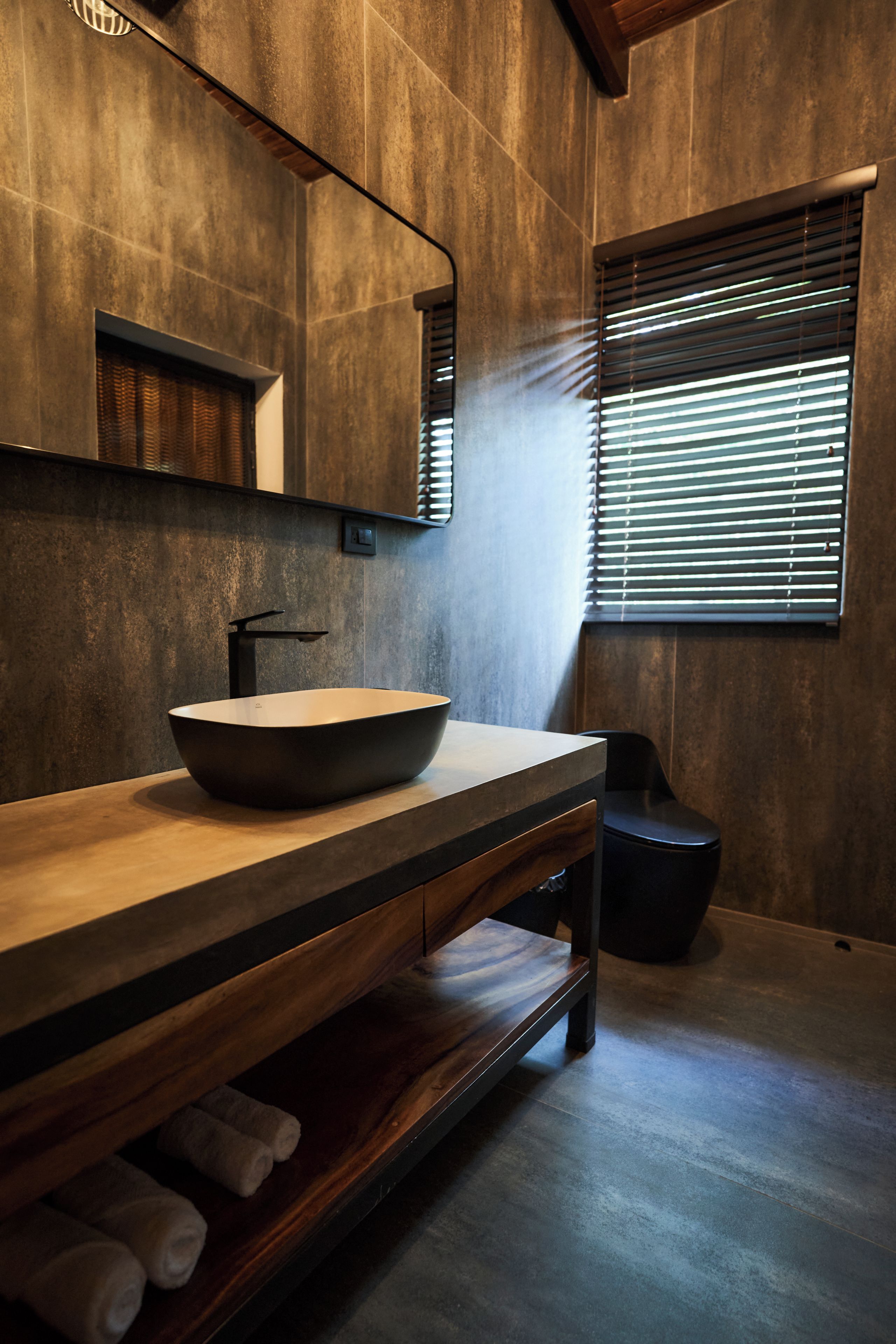 A modern bathroom with a wooden vanity, a large mirror, and a window with blinds.