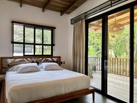 A bedroom with a bed, a window with blinds, and a view of a balcony.