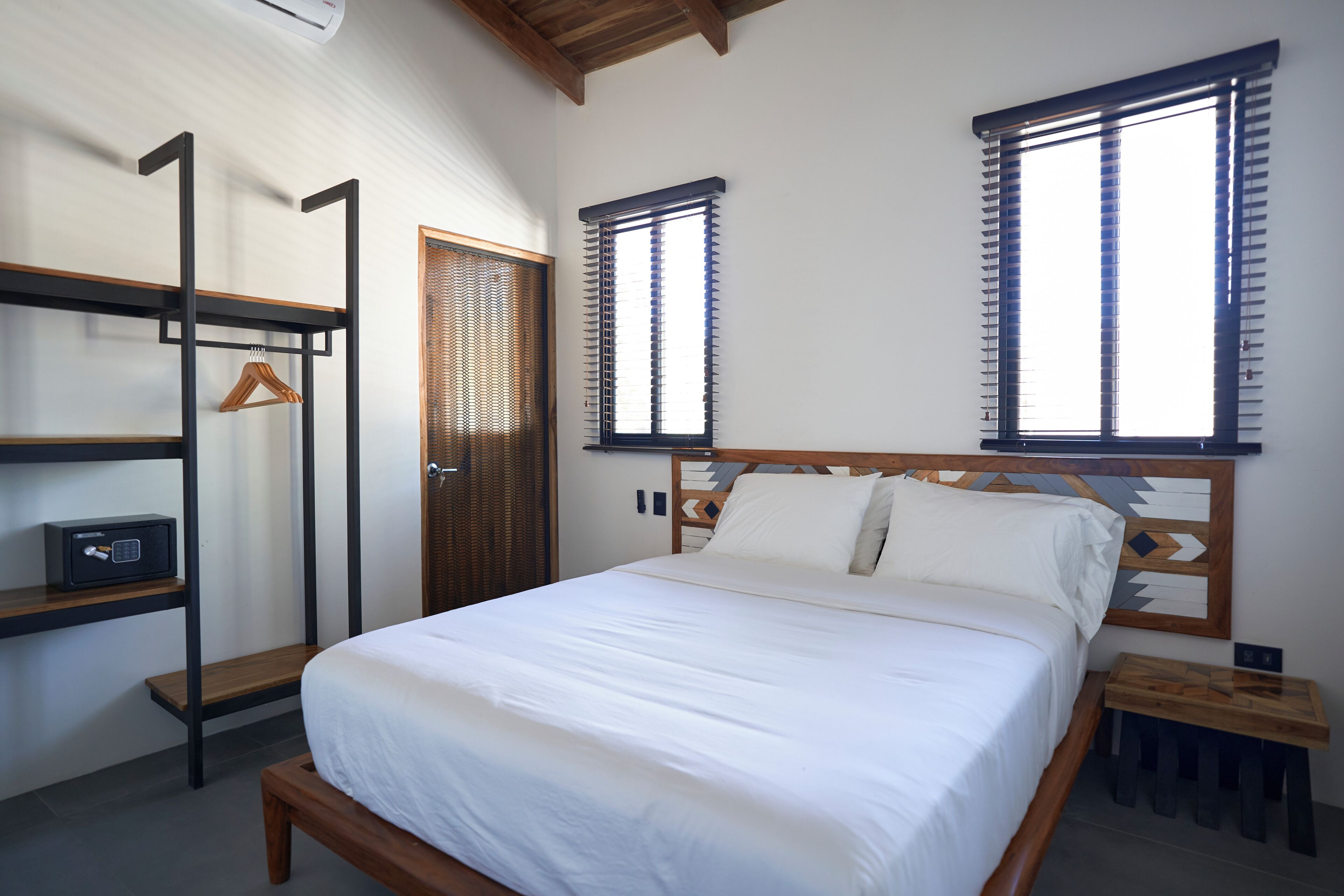 A bedroom with a bed, a wardrobe, a bedside table, and a window with blinds.