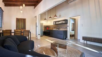 Amplia sala de estar con un sofá moderno, una mesa de centro de vidrio y un comedor. Se ve una cocina al fondo con horno empotrado y un botellero.