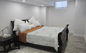 Een slaapkamer met een bed, nachtkastje, bureau en raam.