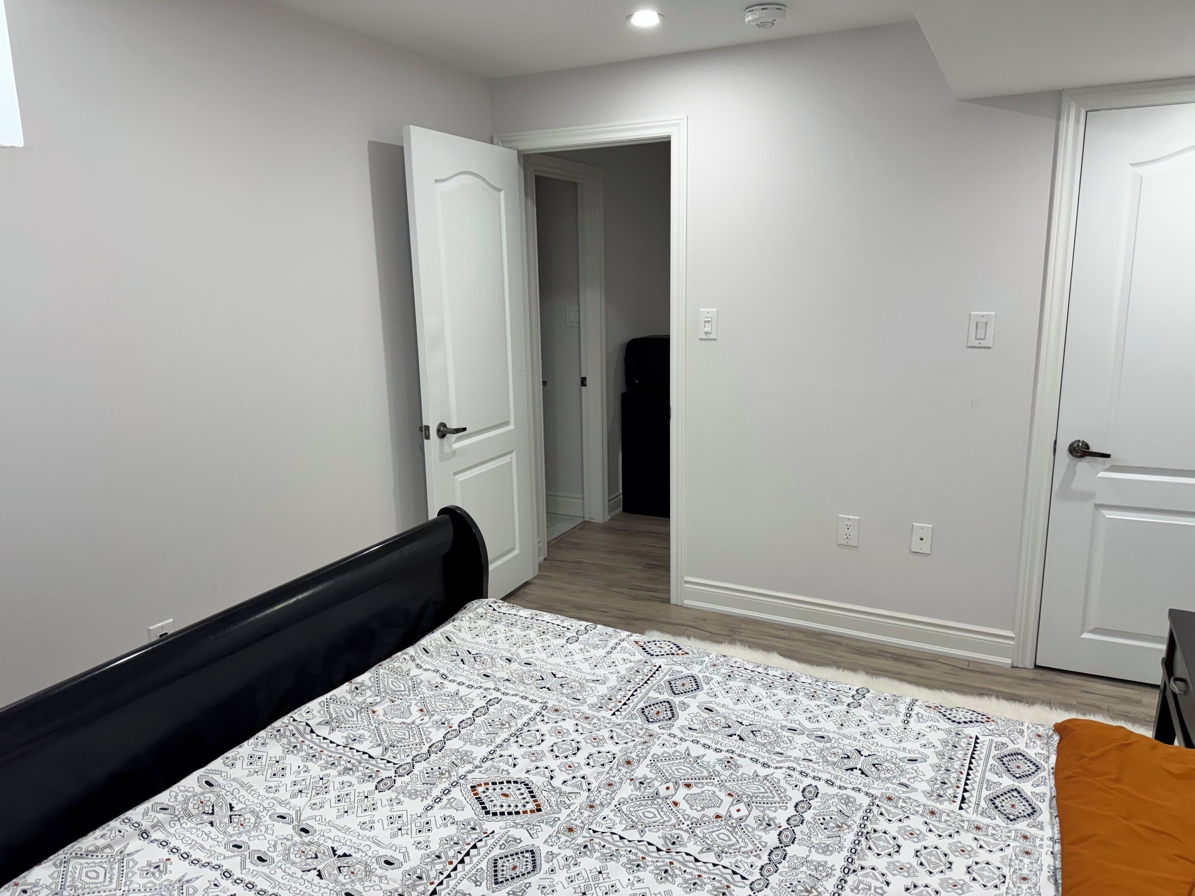 A bedroom with a bed, a door, and a hallway leading to another room.