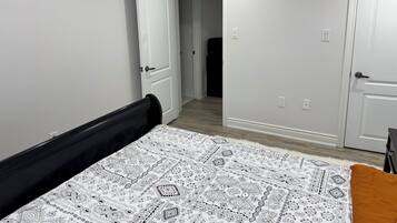A bedroom with a bed, a door, and a hallway leading to another room.
