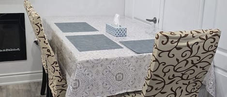 A dining area with a table covered in a patterned tablecloth, surrounded by chairs with a matching design.