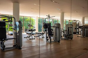 Ein Fitnessstudio mit verschiedenen Trainingsgeräten, großen Fenstern und einem Holzboden.