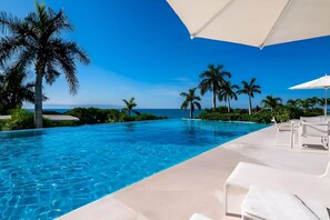 An infinity pool with clear blue water, surrounded by palm trees and a white umbrella. - Amazing 3 Bedroom at Bolongo (Punta de Mita)