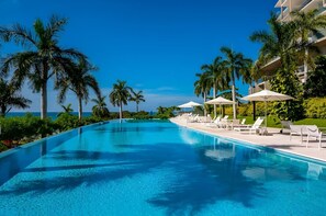 A clear blue pool with lounge chairs and umbrellas, surrounded by palm trees and a clear sky. - Amazing 3 Bedroom at Bolongo (Punta de Mita)