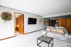 Ein modernes Wohnzimmer mit einer weißen Couch, einem Couchtisch und einem an der Wand befestigten Fernseher.