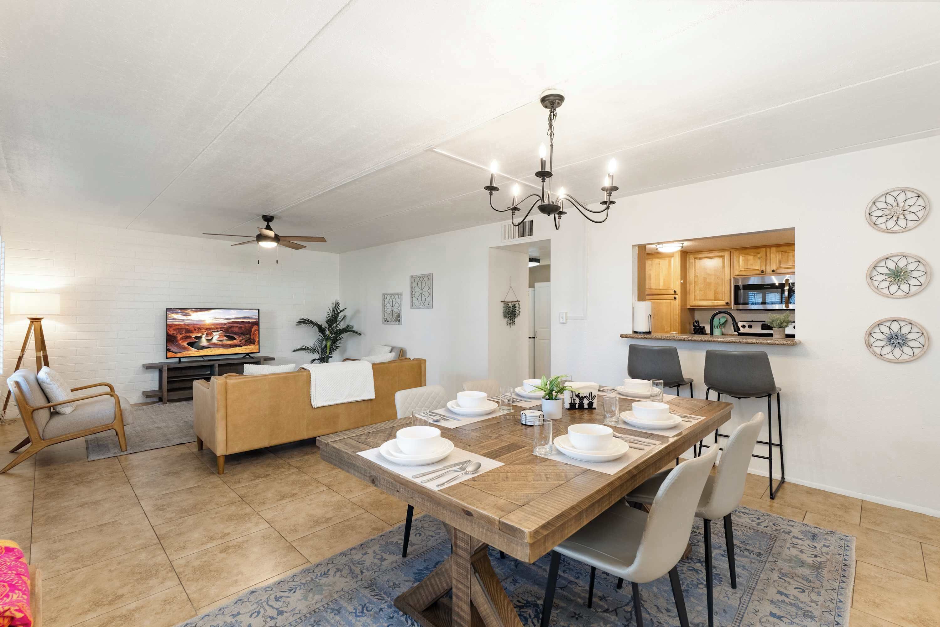 A dining area with a wooden table set for four, a television in the background, and a kitchen visible through an open doorway.