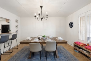 A dining area with a wooden table set for four, surrounded by chairs, a chandelier, and a white brick wall. - Litchfield Park Getaway and Pool 2BR Condo (Litchfield Park)