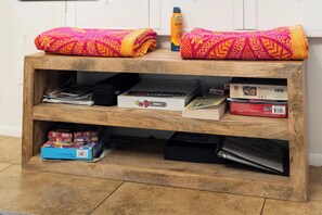 A wooden shelf unit with various items on it, including books, a board game, and a bottle of lotion. - Litchfield Park Getaway and Pool 2BR Condo (Litchfield Park)