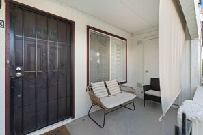 A covered porch with a sliding door, a wicker chair, and a cushioned bench. - Litchfield Park Getaway and Pool 2BR Condo (Litchfield Park)