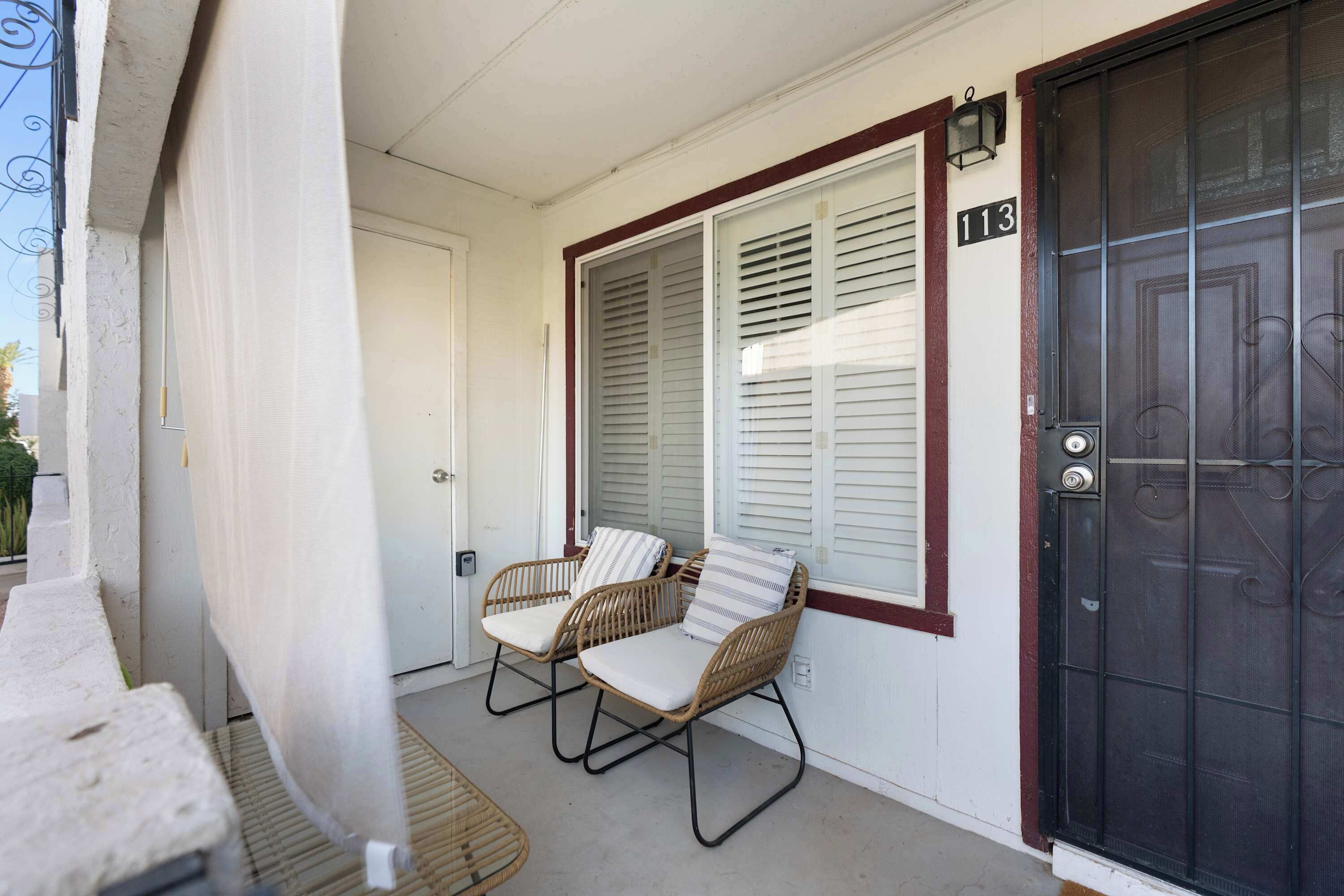 A porch with two wicker chairs and a door with a number plate.