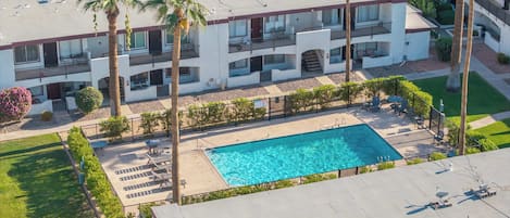 A multi-story hotel with a rooftop pool, palm trees, and a parking area.