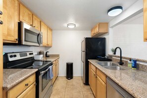 A kitchen with wooden cabinets, a stainless steel refrigerator, a microwave, a stove, and a sink. - Litchfield Park Getaway and Pool 2BR Condo (Litchfield Park)