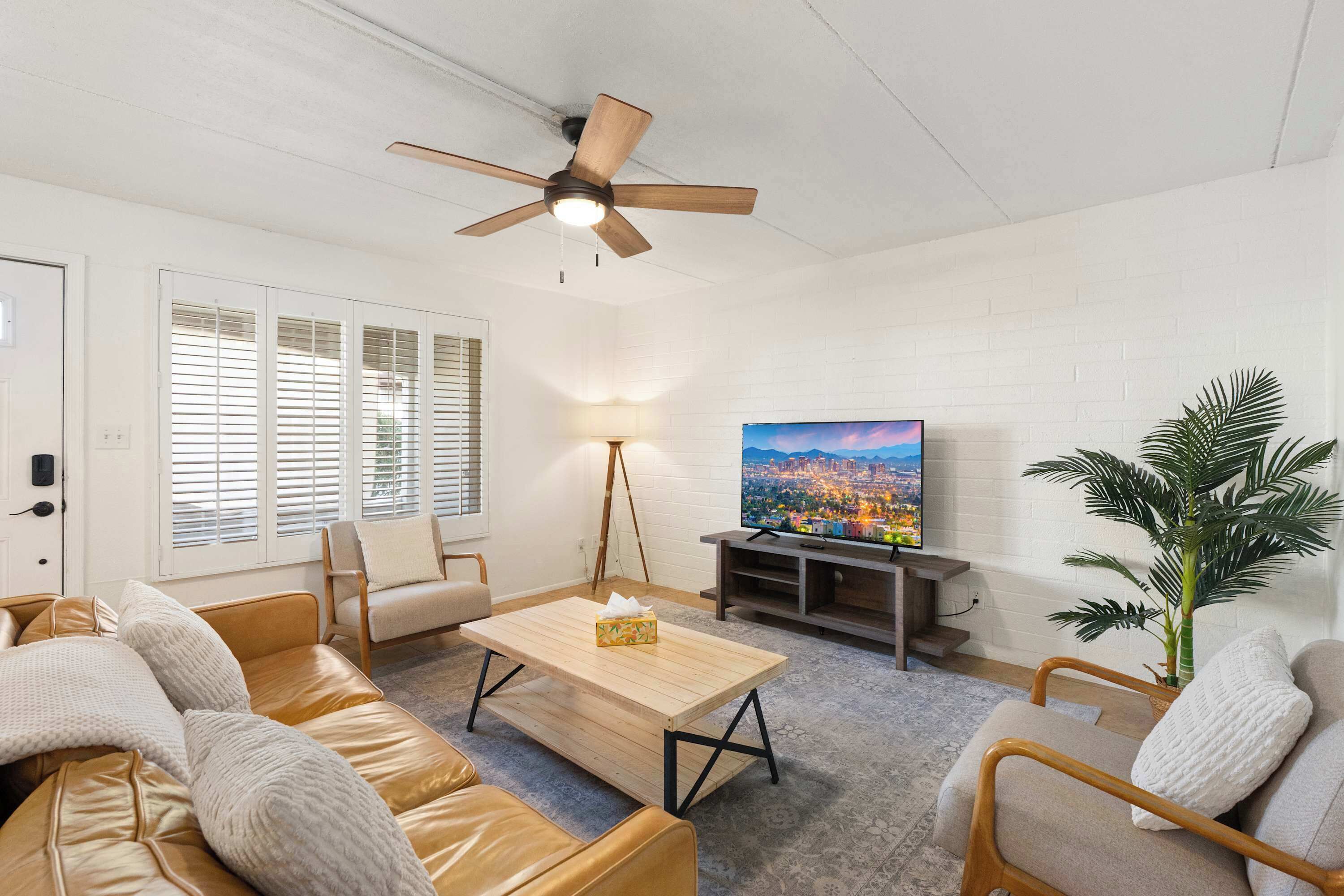 A living room with a ceiling fan, a television, and a large window with blinds.