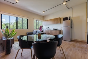 A modern kitchen with a built-in oven and microwave, a dining area with a glass table and black chairs, and large windows offering a view of greenery. - 2 bedrooms, 2 bathrooms | Polanco | Relax (Ciudad de México)