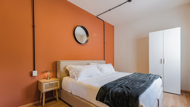 Una camera da letto con un letto, un comodino con una lampada, un armadio e uno specchio a parete.