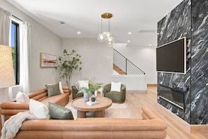 Un salon moderne avec un canapé d’angle, une table basse ronde et un grand téléviseur à écran plat fixé sur un mur en marbre.