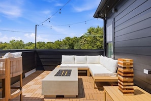 A rooftop patio with a sofa, a fire pit, and a wooden bench.