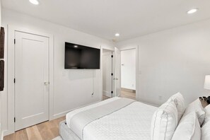A bedroom with a bed, a television mounted on the wall, and a door leading to another room.