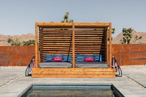 Eine Holzterrasse mit Pool im Vordergrund und einer Wüstenlandschaft im Hintergrund, sowie ein Holenzaun.