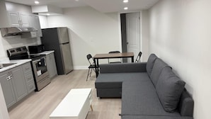 Et moderne køkken med indbyggede hårde hvidevarer, en grå hjørnesofa og et hvidt sofabord.