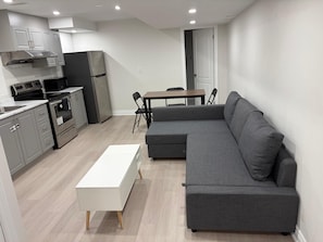A modern kitchen with built-in appliances, a grey sectional sofa, and a white coffee table. - Charming Basement Suite | Near Airport & Wonderland (Brampton)