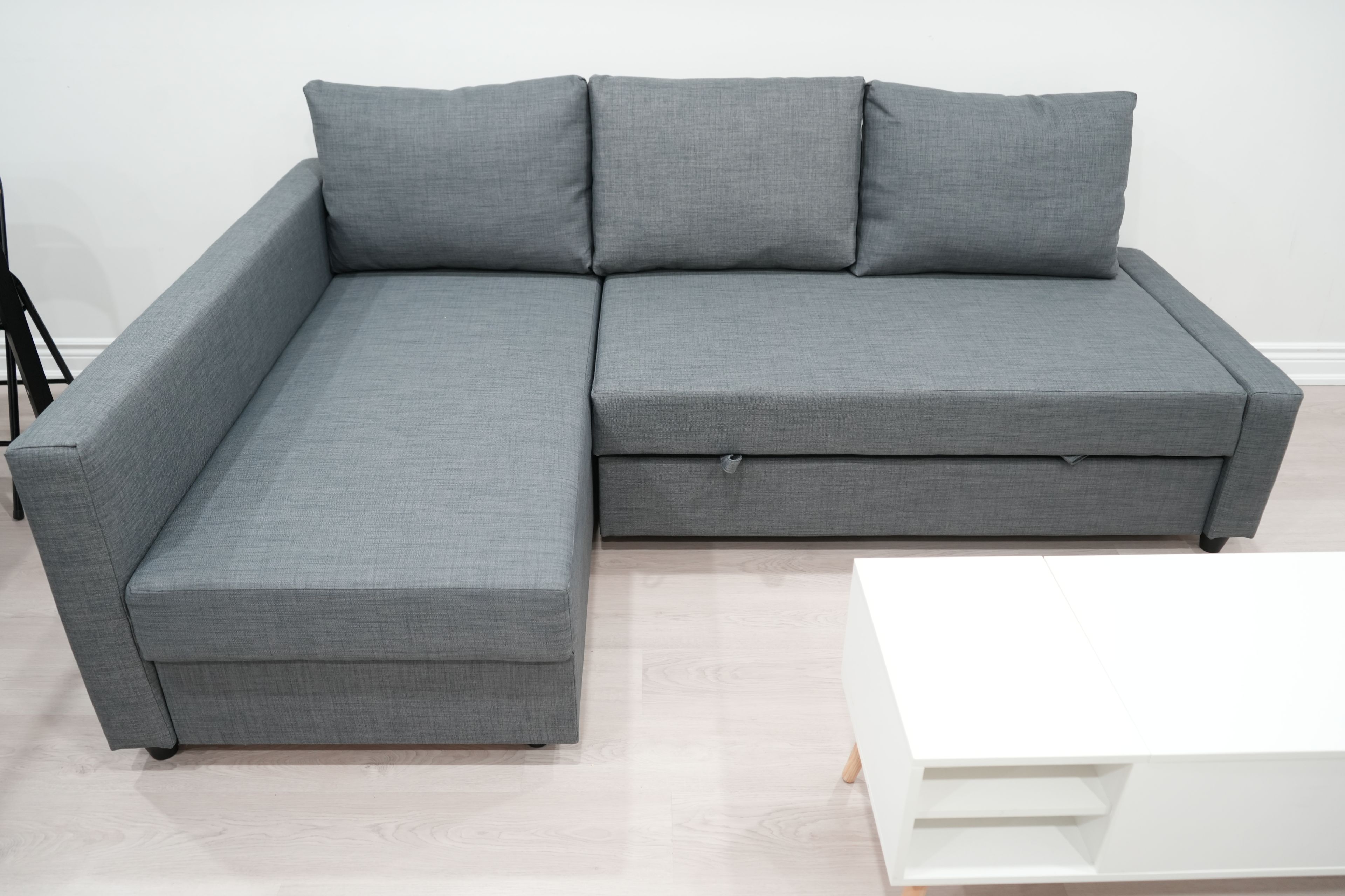 Ein graues Ecksofa mit Chaiselongue, ein weißer Couchtisch und eine schwarze Stehlampe in einem Raum mit hellem Holzboden.