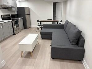 A modern kitchen with a dining area, a grey sofa, and a white coffee table. - Charming Basement Suite | Near Airport & Wonderland (Brampton)