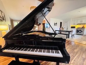 A grand piano in a well-lit room with a dining area and kitchen in the background. - Spacious UGA Game Day Home w/ Piano - Athens GA 10 Min to Stadium (Athens)