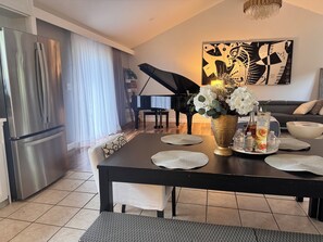 A modern kitchen with a stainless steel refrigerator, a dining table with placemats, a vase with flowers, and a piano in the background. - Spacious UGA Game Day Home w/ Piano - Athens GA 10 Min to Stadium (Athens)