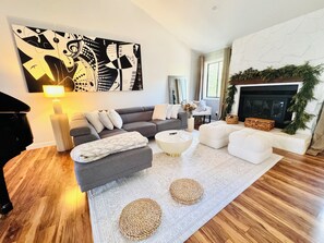 A modern living room with a grey sofa, white pouf, and a large abstract painting. - Spacious UGA Game Day Home w/ Piano - Athens GA 10 Min to Stadium (Athens)
