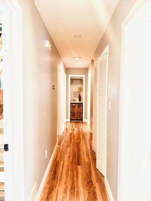 A hallway with wooden flooring, white walls, and a door leading to a room with a cabinet and decorative items. - Spacious UGA Game Day Home w/ Piano - Athens GA 10 Min to Stadium (Athens)