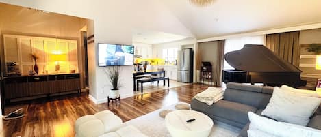 A modern living room with a sofa, ottomans, a coffee table, a television, and a piano.