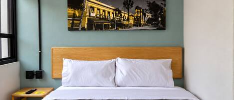 A hotel room with a bed, a nightstand, a wall-mounted picture, and a window.