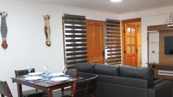 A dining area with a table set for four, a sofa, and a television.