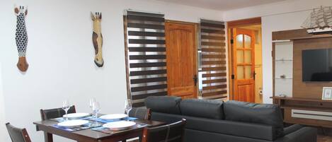 Un área de comedor con una mesa dispuesta para cuatro personas, un sofá y un televisor.