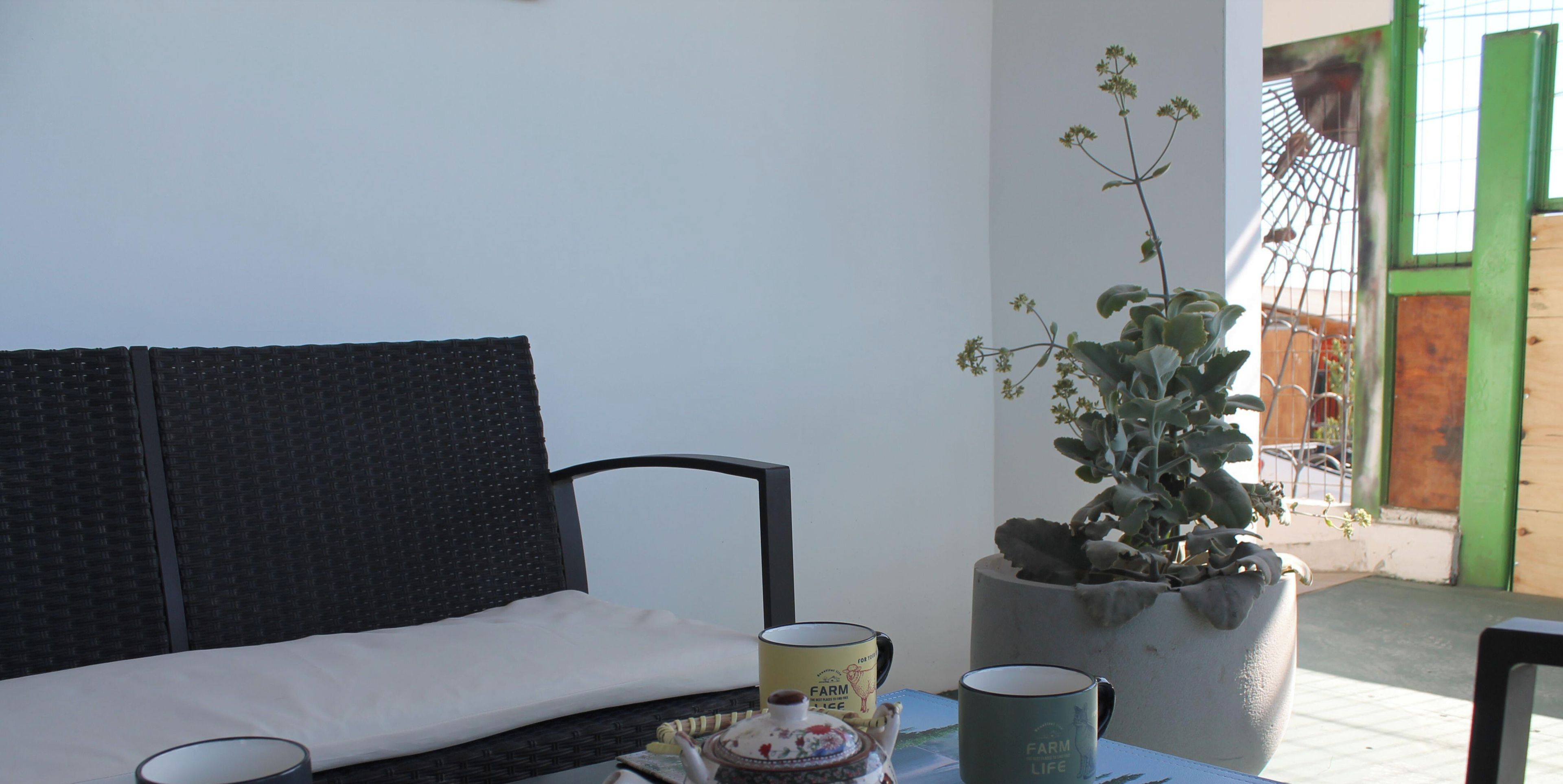 A room with a black sofa, a table with a teapot, cups, and a potted plant.