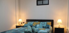 A bed with a patterned bedspread, two bedside lamps, and a nightstand with a lamp. - Disegni 22 · Caldera Family Department (Caldera)