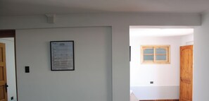 A hallway with a framed notice on the wall, a wooden door, and a window with a wooden frame. - Disegni 22 · Caldera Family Department (Caldera)