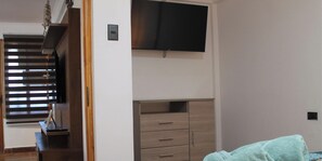 A room with a wooden staircase, a flat-screen TV mounted on the wall, and a set of drawers. - Disegni 22 · Caldera Family Department (Caldera)